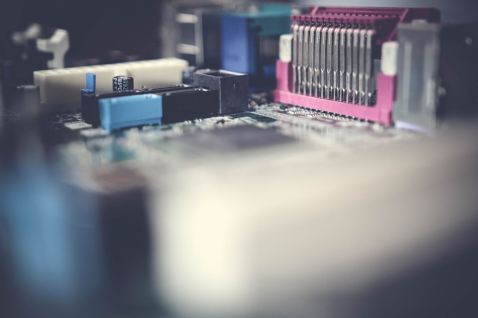Foto macro de uma placa-mãe de computador com slots e capacitores, com o primeiro plano bem desfocado.